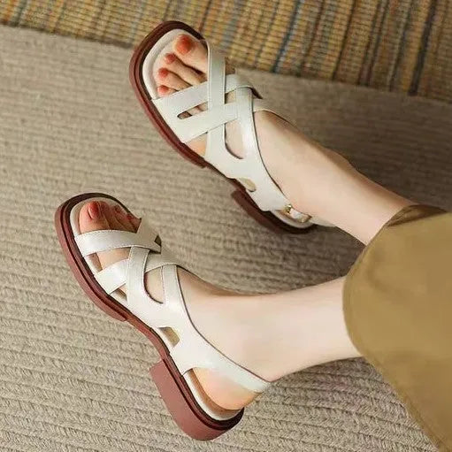 Glossy black patent leather women's sandals with a square toe and ankle strap on a flat rubber sole.