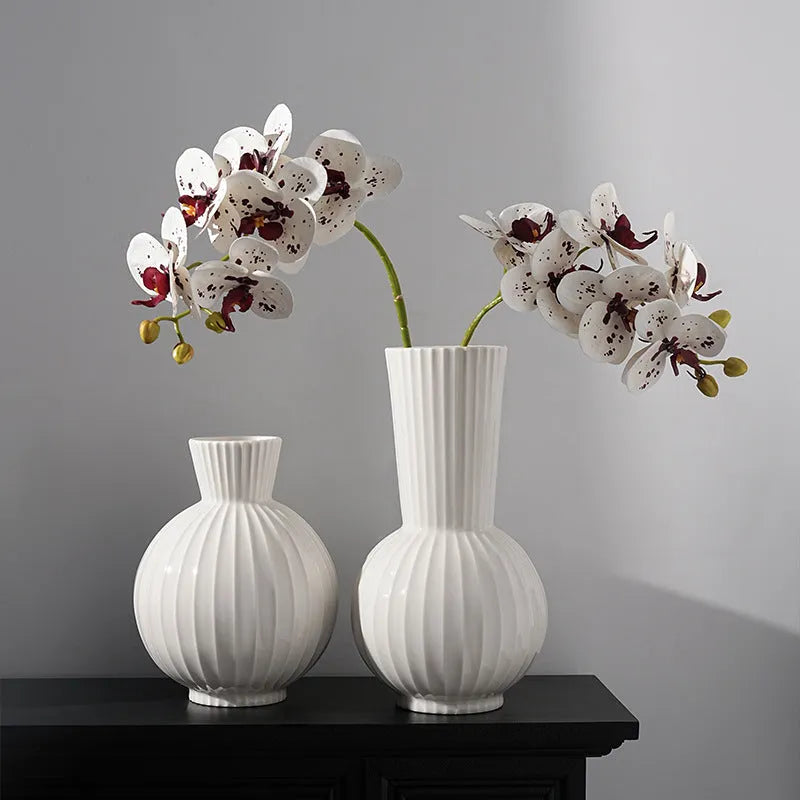 White ceramic ball vase with vertical stripes on a wooden table, with optional artificial purple orchid stems.