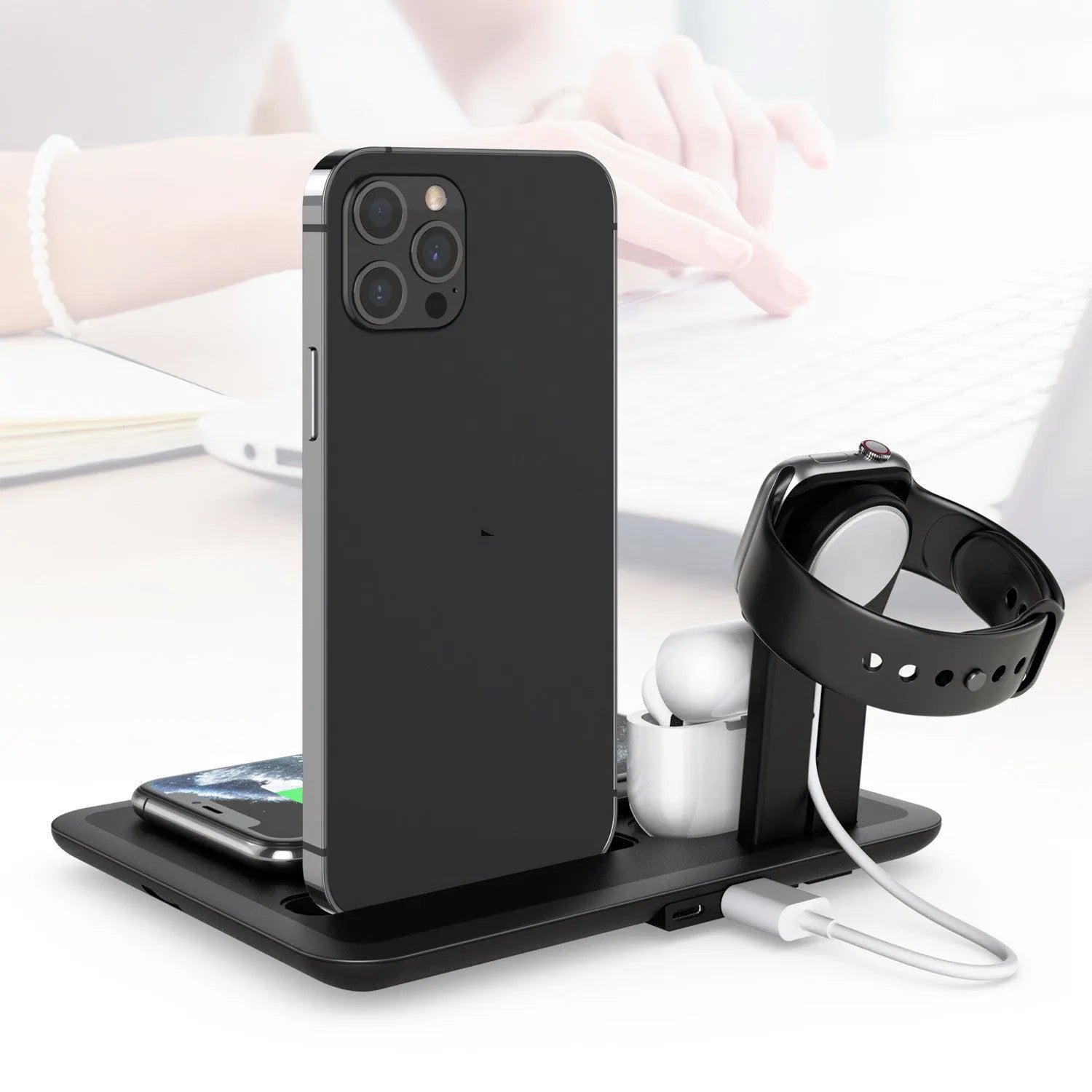 Black desktop wireless charging station with phone on pad, watch in bracket, and headphones on hook.
