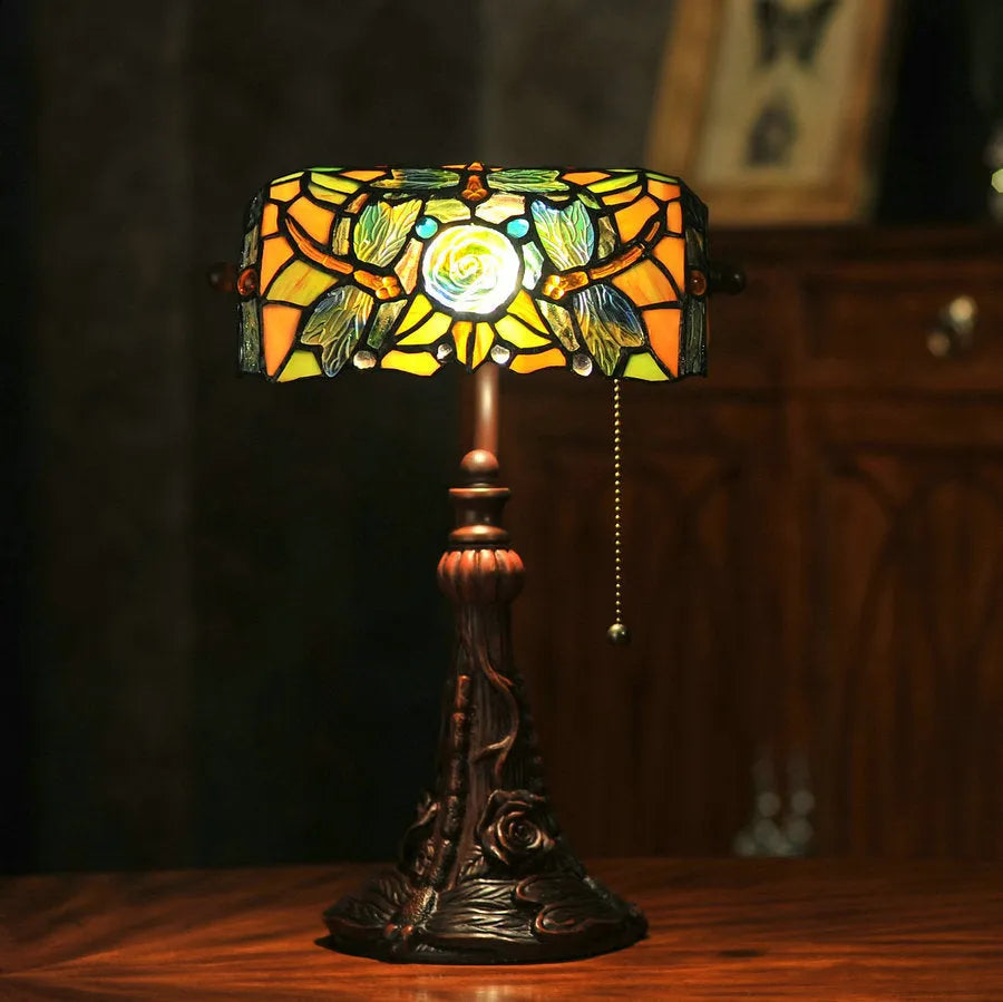 Tiffany-style table lamp with coloured glass shade and resin base on a wooden desk.