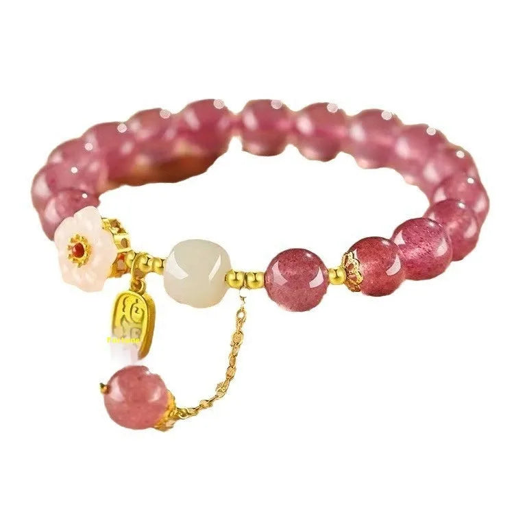 Handmade strawberry quartz crystal bracelet with peach blossom charms on a wrist.