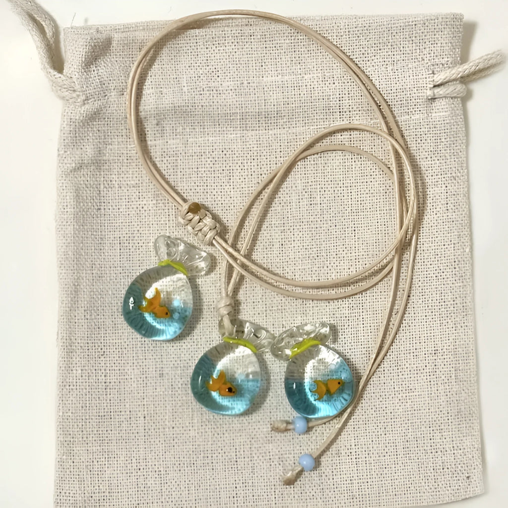 Women's necklace with blue glazed small fish charm pendant on a beige cotton-linen clavicle chain.