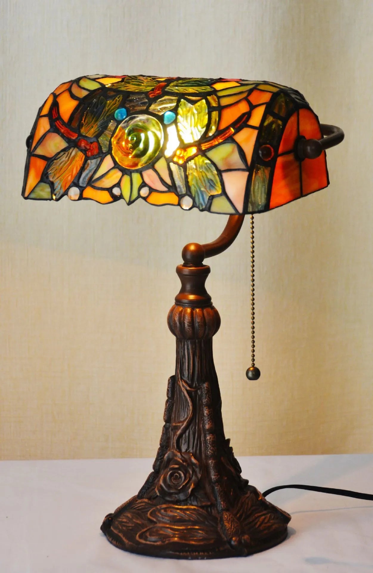 Tiffany-style table lamp with coloured glass shade and resin base on a wooden desk.