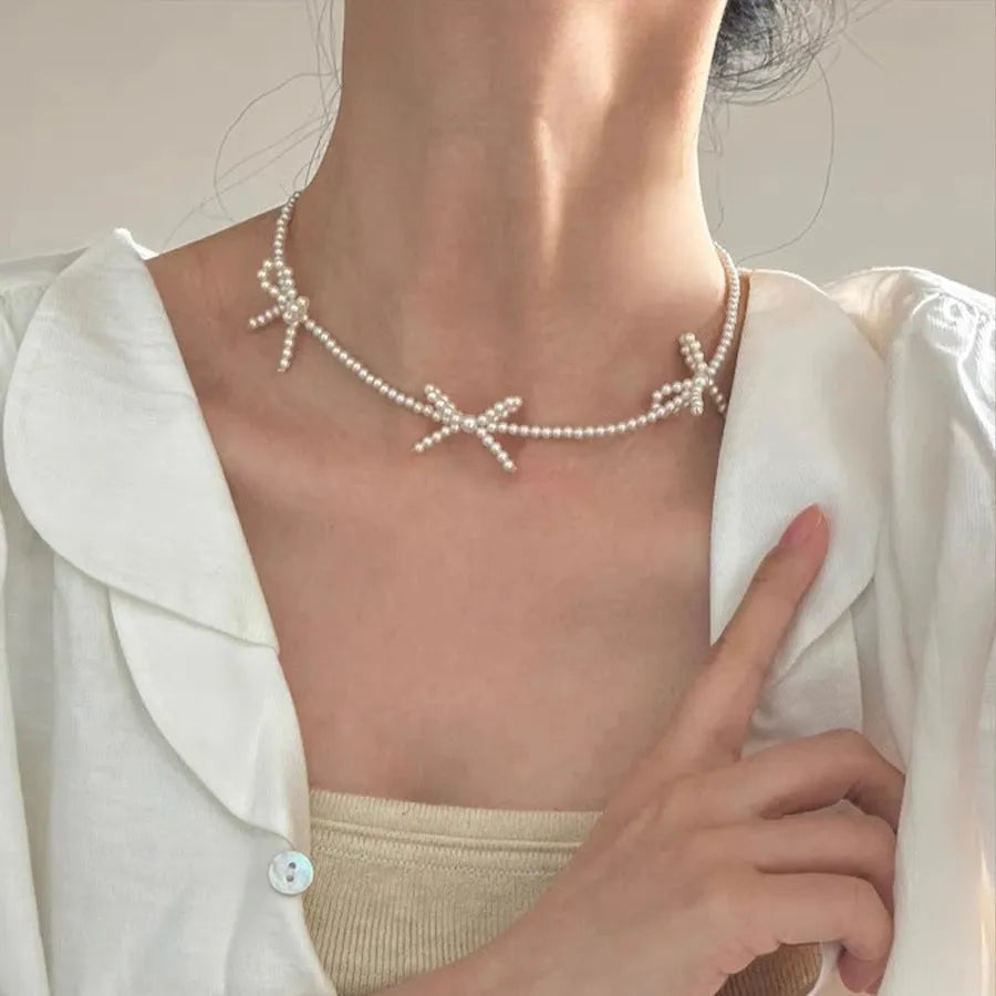 White imitation pearl necklace with a geometric bow charm on an adjustable chain.