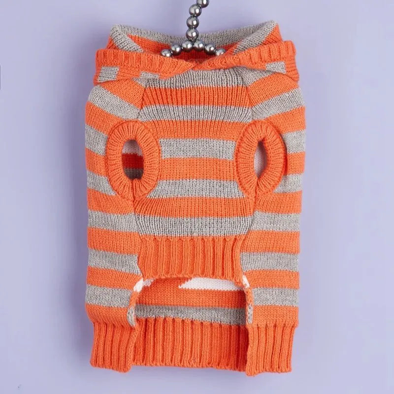 Orange knitted dog sweater with striped pattern, fur ball trim, and a hood for Halloween.
